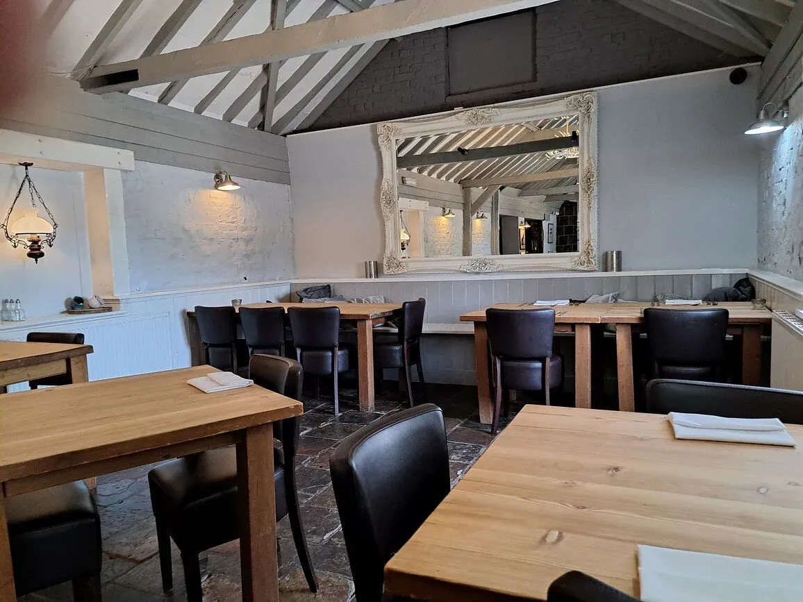 The same white vaulted room arranged with long tables and dark chairs, a large framed mirror on the end wall.